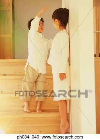 Stock Image - Young brother measuring height of sister. Fotosearch