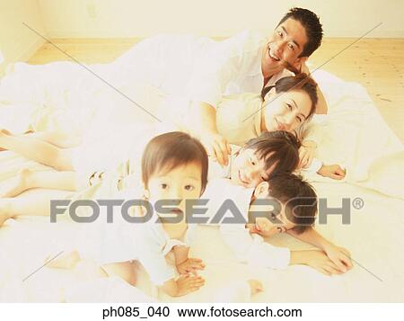 Stock Image - Family lying on bed together. Fotosearch