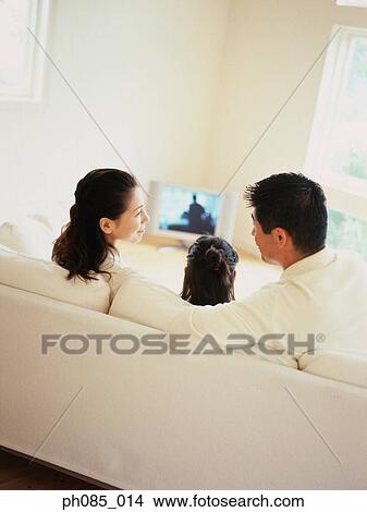 Parents and daughter watching television, rear view View Large Photo Image Picture - Parents and daughter watching television, rear view. Fotosearch