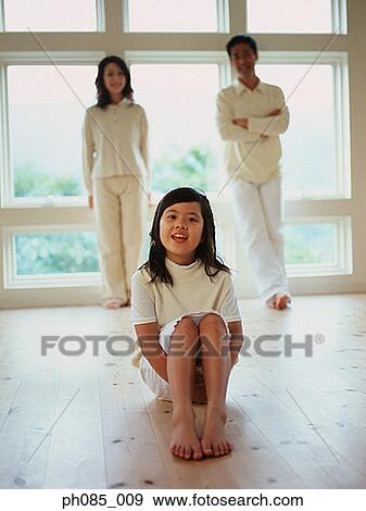 Young girl sitting on ground, parents standing in background View Large Photo Image Stock Photo - Young girl sitting on ground, parents standing in background. Fotosearch