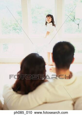 Young girl standing by window looking back, parents in foreground View Large Photo Image Stock Image - Young girl standing by window looking back, parents in foreground. Fotosearch