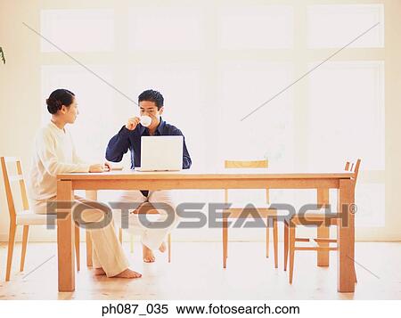 Couple sitting at table, man drinking coffee View Large Photo Image Stock Photography - Couple sitting at table, man drinking coffee. Fotosearch