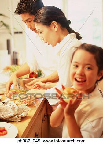 Father and mother in kitchen preparing food, daughter holding an onion View Large Photo Image Stock Photo - Father and mother in kitchen preparing food, daughter holding an onion. Fotosearch
