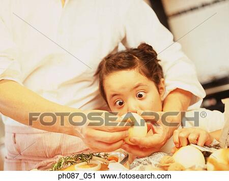 Stock Image - Father peeling onion, daughter look with eyes open wide. Fotosearch