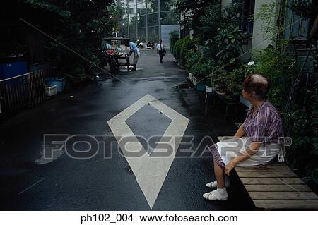 Picture - Matured Japanese woman sitting on a bench, in an alley. Fotosearch