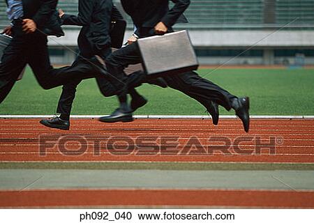 Stock Image - Businessmen running on stadium track, carrying briefcases, low section. Fotosearch