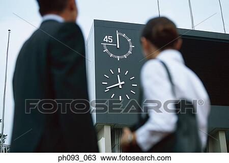 Stock Image - Business people looking at clock on stadium sign display. Fotosearch