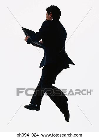 Picture - Young businessman leaping in air, holding a computer notebook. Fotosearch