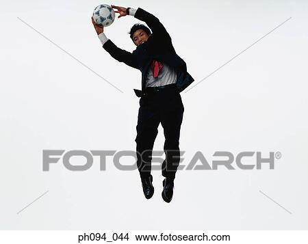 Picture - Young businessman leaping in air, holding a soccer ball. Fotosearch