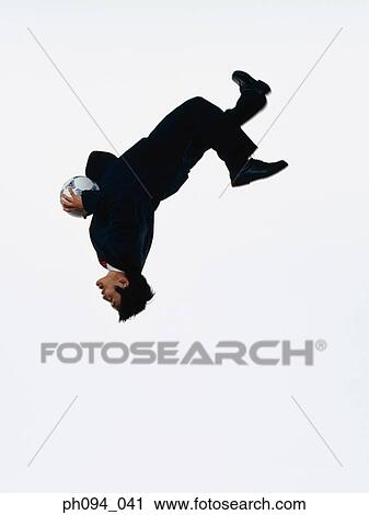 Stock Image - Young businessman leaping in air, holding a soccer ball. Fotosearch