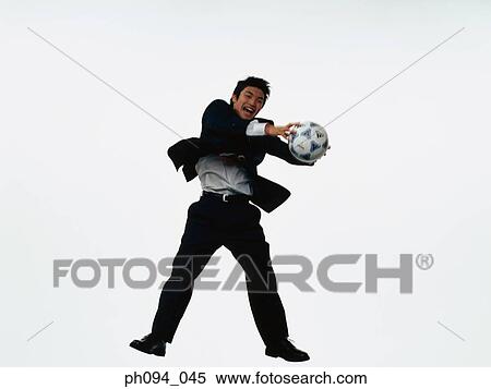 Stock Photography - Young businessman leaping in air, holding a soccer ball. Fotosearch