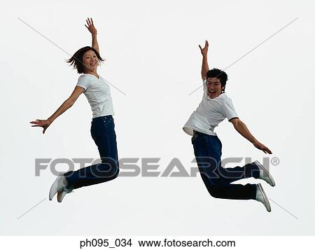 Two young Asian man and woman in jeans & t-shirt, jumping in mid-air View Large Photo Image Picture - Two young Asian man and woman in jeans & t-shirt, jumping in mid-air. Fotosearch
