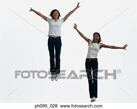Stock Photo - Two young Asian women in jeans & t-shirt, jumping in mid-air. Fotosearch