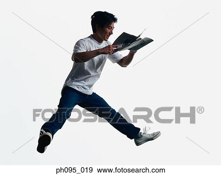 Stock Photo - Young Asian man in jeans & t-shirt, and newspaper, jumping in mid-air. Fotosearch