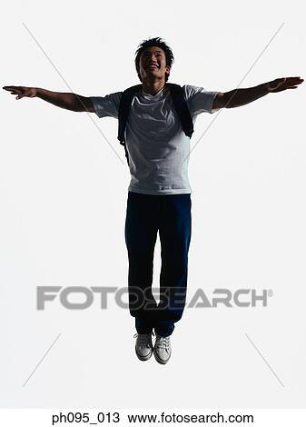 Stock Image - Young Asian man in jeans & t-shirt, carrying haversack, jumping in mid-air. Fotosearch