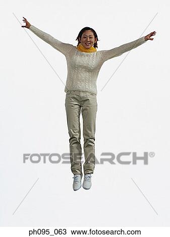 Stock Image - Young Asian woman in pants & sweat-shirt and scarf, jumping in mid-air. Fotosearch