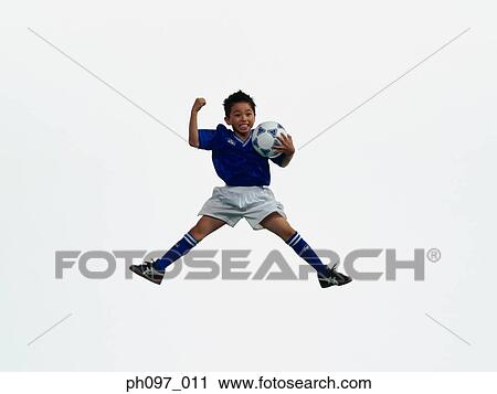 Stock Image - Young Asian boy holding football, jumping in mid-air. Fotosearch