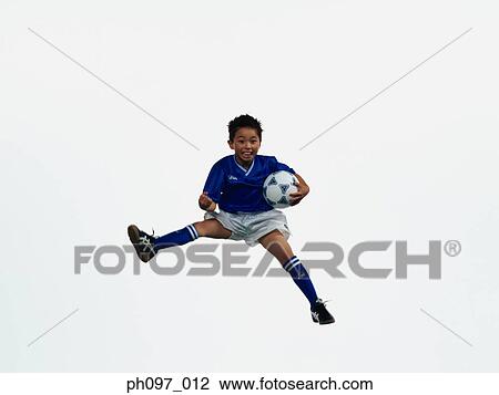 Stock Image - Young Asian boy holding football, jumping in mid-air. Fotosearch