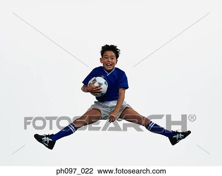 Stock Image - Young Asian boy holding football, jumping in mid-air. Fotosearch