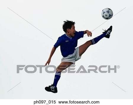 Stock Photography - Young Asian boy kicking football in mid air. Fotosearch