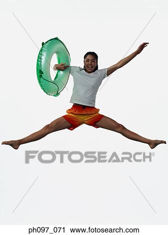 Stock Image - Young Asian girl holding inflated ring, jumping in mid-air. Fotosearch