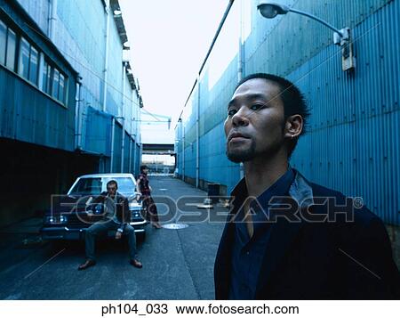 Man standing, a couple beside a car in background View Large Photo Image Stock Image - Man standing, a couple beside a car in background. Fotosearch