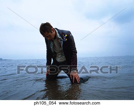 Picture - Man kneeling at the beach in pain. Fotosearch