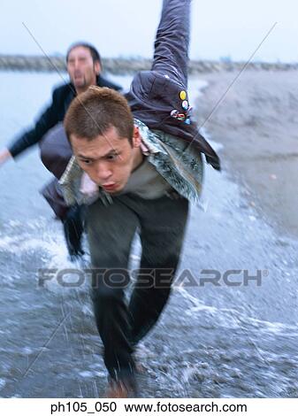 Stock Image - Two men in a chase at the beach. Fotosearch