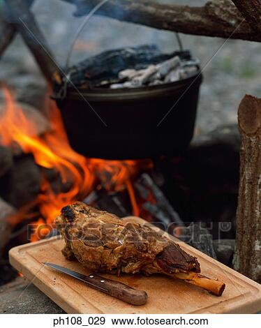 Leg of beef on chopping board, pot over fire in background View Large Photo Image Stock Photo - Leg of beef on chopping board, pot over fire in background. Fotosearch