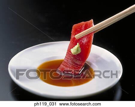 Stock Image - Dipping a slice of raw fish in soya sauce. Fotosearch