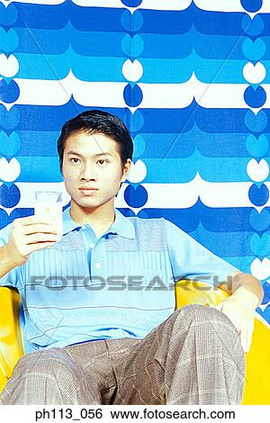 Stock Photograph - Man sitting on yellow ball chair holding a glass of milk. Fotosearch