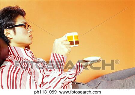 Young man relaxing on couch, holding saucer and cup View Large Photo Image Stock Photo - Young man relaxing on couch, holding saucer and cup. Fotosearch