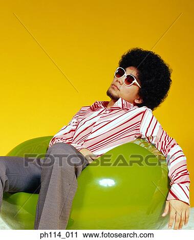 Stock Image - Young Asian male with afro hair in sitting on ball chair. Fotosearch