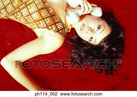 Stock Image - Young woman on the phone, lying on carpeted floor. Fotosearch