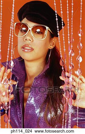 Picture - Young woman wearing sunglass standing behind beaded curtain. Fotosearch