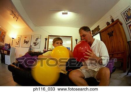 Stock Image - Father and son blowing balloons. Fotosearch