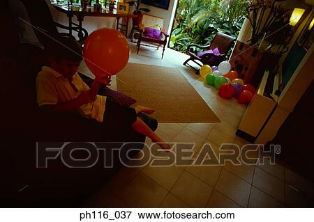 Young boy resting on wooden chair holding a balloon View Large Photo Image Stock Photo - Young boy resting on wooden chair holding a balloon. Fotosearch