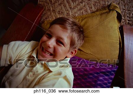 Young boy resting on wooden chair, smiling View Large Photo Image Stock Photograph - Young boy resting on wooden chair, smiling. Fotosearch