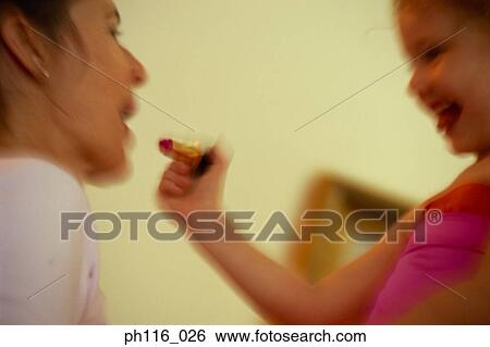Stock Photograph - Young daughter putting on lipstick for Mother. Fotosearch