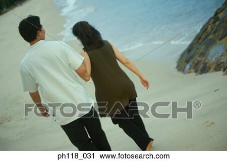Couple walking along beach, rear view View Large Photo Image Stock Image - Couple walking along beach, rear view. Fotosearch