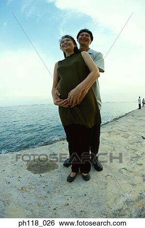 Stock Photograph - Portrait of a man hugging a pregnant woman . Fotosearch