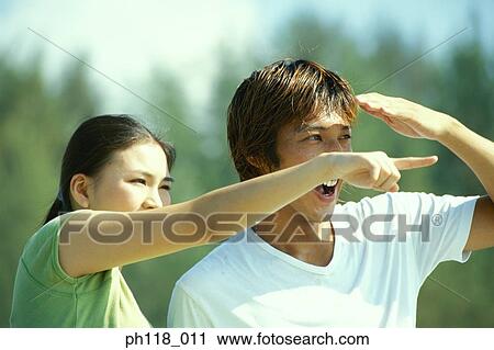 Stock Image - Young couple on beach, woman pointing . Fotosearch