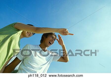 Stock Image - Young couple on beach, woman pointing . Fotosearch