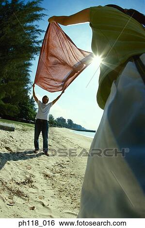 Stock Photograph - Young couple spreading fabric on beach. Fotosearch