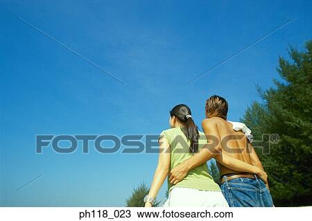 Stock Image - Young couple walking along beach, rear view. Fotosearch
