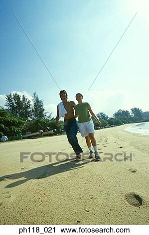 Stock Image - Young couple walking along beach. Fotosearch