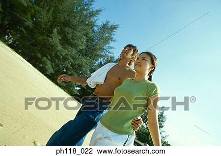 Stock Image - Young couple walking along beach. Fotosearch