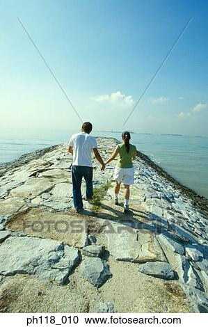 Young couple walking on water breaker, rear view View Large Photo Image Stock Image - Young couple walking on water breaker, rear view . Fotosearch