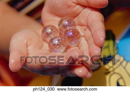 Stock Image - Hands cupped, holding crystal-like marbles. Fotosearch