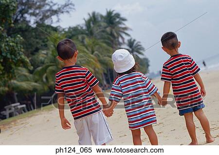 Stock Photography - Rear view of 2 boys and a girl at the beach holding hands. Fotosearch